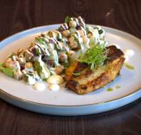 A plate with a grilled piece of paneer garnished with greens alongside a chickpea salad topped with dressing, served on a wooden table.