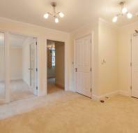 Unfurnished interior hallway with beige carpet, cream walls, three doors, a windowed door, and ceiling lights.