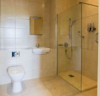 Modern bathroom with beige tiles, a wall-mounted toilet, a small sink with mirror, and a glass-enclosed shower area with chrome fixtures.
