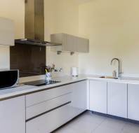 Modern kitchen with light-colored cabinets, a microwave, stovetop, hood, kettle, and sink, all set against a clean countertop and cream walls.