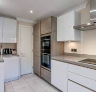 Modern kitchen with white cabinets, built-in double ovens, electric cooktop, small appliances on the counter, and a closed white door in the background.