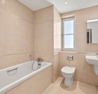 Modern bathroom with beige tiles, a built-in bathtub, wall-mounted toilet, rectangular sink, mirrored cabinet, and a frosted window.