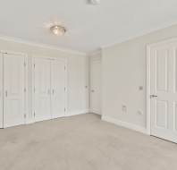 Empty room with beige carpet, white walls, three closed white doors, and a ceiling light fixture.