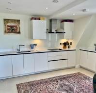 Modern white kitchen with flat-panel cabinets, built-in appliances, a patterned rug on the floor, and decorative items on the walls and upper cabinets.