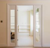 White double glass doors open into a small, beige room with carpet, built-in shelves, and a window on the right wall.