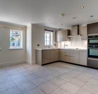Modern, empty kitchen with glossy cabinets, built-in ovens, tiled floor, and large windows letting in natural light.