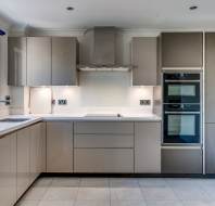 Modern kitchen with glossy beige cabinets, built-in oven and microwave, stainless steel vent hood, and large window above the sink.