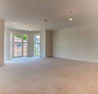 Spacious empty room with beige carpet, white walls, ceiling lights, and large bay windows letting in natural light.