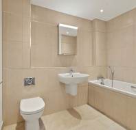 Modern bathroom with beige tiles, wall-mounted toilet, white sink, bathtub with shower attachment, mirrored cabinet, and heated towel rail.