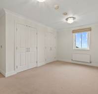 Empty, carpeted room with cream walls, a window with a shade, two light fixtures, two double-door closets, and an open doorway leading to another room.