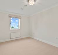 Empty room with beige carpet, white walls, a window with a blind, a ceiling light fixture, radiator, and electrical outlets.