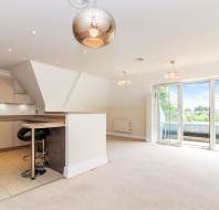 Modern open-plan kitchen and living area with beige cabinets, breakfast bar, pendant lights, and large sliding glass doors leading to a balcony with a scenic outdoor view.