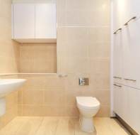 Modern bathroom with beige tiles, a wall-mounted sink, a toilet, white cabinets, and a washing machine in the corner.