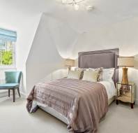 A modern bedroom with a double bed, two bedside tables with lamps, a blue chair by the window, and a light fixture on the ceiling.