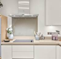 Modern kitchen with white cabinets, built-in oven, electric cooktop, range hood, and countertop items including utensils, flowers, books, wine glasses, and a bowl.