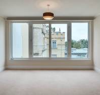 Unfurnished room with beige carpet, large window, and view of a stone building with turret and greenery outside. Ceiling light fixture is centered.