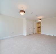 Spacious, empty room with beige carpet, white walls, two ceiling lights, large window, built-in closets, and an open door leading to a bathroom.