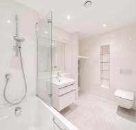 Modern white bathroom with a bathtub, wall-mounted shower, large mirror, sink with vanity, wall-mounted toilet, and built-in shelving.