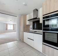 Modern kitchen with light wood and white cabinets, built-in oven and microwave, electric cooktop, and a view into a bright adjacent living room.