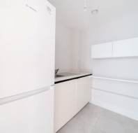 A modern, minimalistic kitchen featuring a white Bosch refrigerator, white cabinets, a countertop with a sink, and light gray tiled flooring.