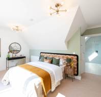 Bright modern bedroom with a double bed, orange and green accents, artwork of a bird, dressing table, and en-suite bathroom visible through an open door.