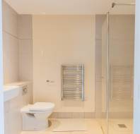 Modern bathroom with a wall-mounted toilet, white sink, towel radiator, glass shower enclosure, and a bath mat on a tiled floor.