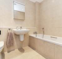 Modern bathroom with beige tiles, wall-mounted sink, mirror cabinet, toilet, towel ring with gray towel, and a bathtub with a handheld showerhead.