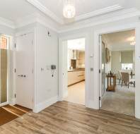 Bright entryway with wood flooring leads to a modern kitchen and dining area. White walls, interior doors, and a bouquet of flowers on the right complete the scene.