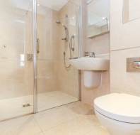 Modern bathroom with beige tiles, a glass walk-in shower, wall-mounted sink, and a wall-mounted toilet.