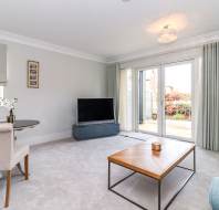 Bright living room with light carpeting, a sofa, coffee table, TV, small dining table with chairs, and glass doors leading to a patio.