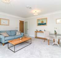 A bright living room with a blue sofa, two chairs at a round table, a wooden coffee table, and framed artwork on white walls.