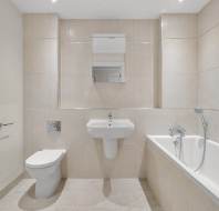 A neutral-toned bathroom featuring a wall-mounted toilet, a pedestal sink with a mirror above, and a bathtub with a handheld shower head.