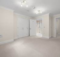 Empty bedroom with beige carpet and cream walls, featuring built-in closet doors and an open doorway leading to an en suite bathroom.