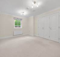 Empty bedroom with cream walls, beige carpet, a single window, and white built-in wardrobes.