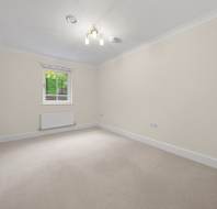 Empty room with beige walls, carpeted flooring, a single window, and a central light fixture.
