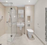 A modern bathroom with a glass walk-in shower, a wall-mounted sink, a toilet, and a chrome towel radiator.