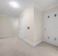 A brightly lit hallway with beige walls, cream carpeting, and three closed white doors.
