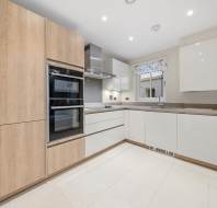 Modern kitchen with light wood floor-to-ceiling cabinets, white lower cabinets, a built-in double oven, and a stainless steel range hood.
