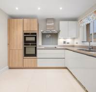 Modern kitchen featuring wood-grain floor-to-ceiling cabinets, a built-in double oven, white gloss cabinets, and light stone countertops.