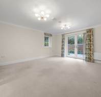 An empty room with beige carpet, cream walls, two chandeliers, a window, and glass patio doors leading to a patio.