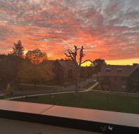 Suburban neighborhood at sunset with an orange and pink cloudy sky above houses and trees.