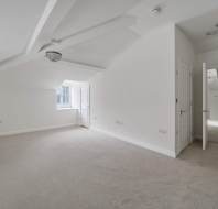 Empty attic bedroom with white walls, carpeted floors, sloped ceilings, and doorways leading to adjacent rooms.