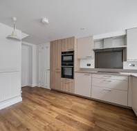 A modern kitchen with light-colored cabinets, a built-in oven, and wood flooring.