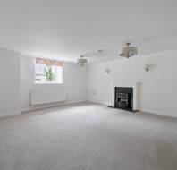 Empty room with white walls, carpeted flooring, a fireplace, and a window with a radiator beneath it.