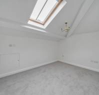An empty attic room with white walls, grey carpet, a sloped ceiling with a skylight, and a small chandelier.