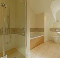 A bathroom featuring a glass-enclosed shower, a built-in bathtub with a wood-finish side panel, a toilet, and a wall-mounted sink beneath a window.