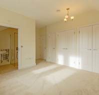 An empty room with cream walls, carpeted flooring, and multiple white paneled doors, with an attached bathroom visible through an open doorway.