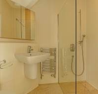 A bathroom with a wall-mounted sink, a chrome towel warmer, and a walk-in glass shower.