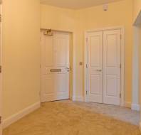 A beige hallway with a single door on the left, a double door on the right, and a wall-mounted intercom.
