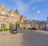 Large stone manor hotel with a parking lot in front containing a grey SUV, a red car, and a golf cart.